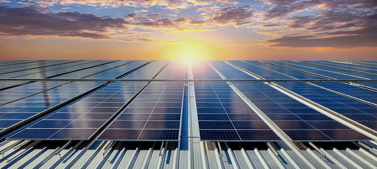 Rows of solar panels on a corrugated metal roof, with the sun setting behind them