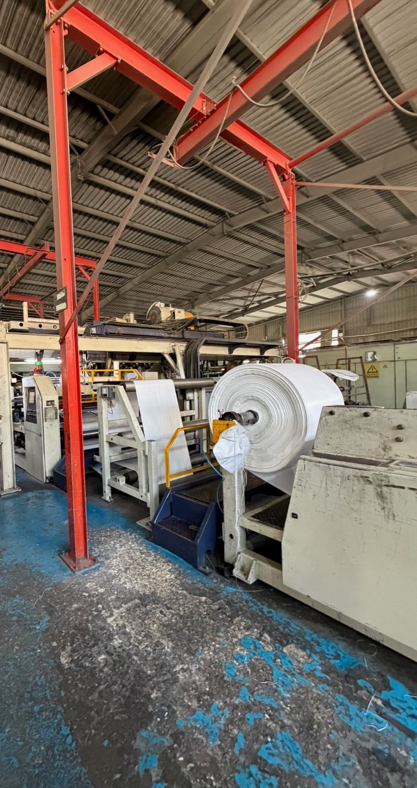 A plastic film line under a red steel gantry, a large roll of white film at its end