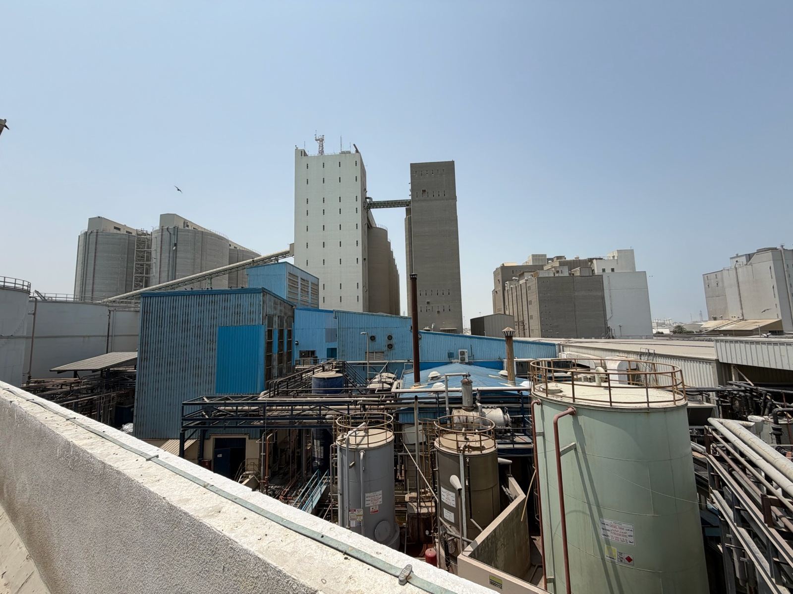 A food plant’s silos, process towers and tanks seen from a rooftop under a hazy blue sky