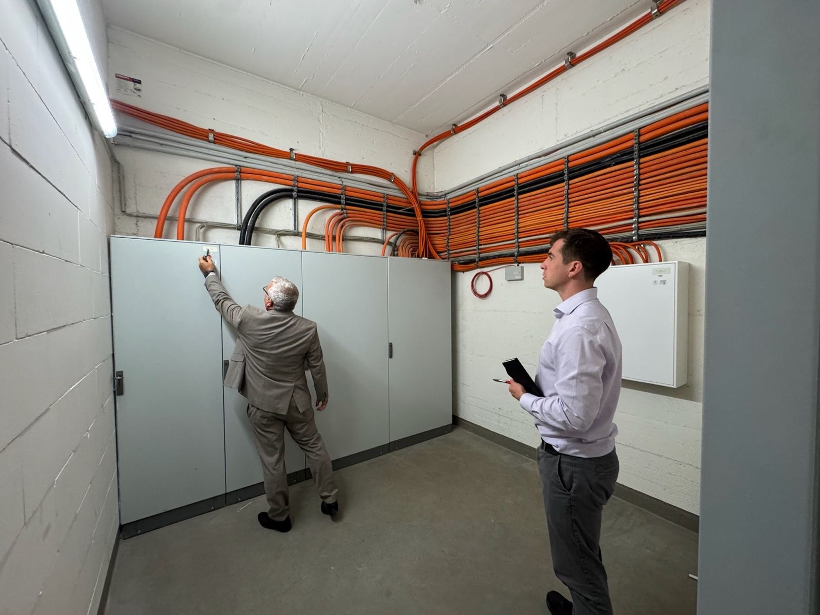A member of the HarmoniQ team with a tablet surveying a hotel switchgear room while a colleague reaches up to a panel