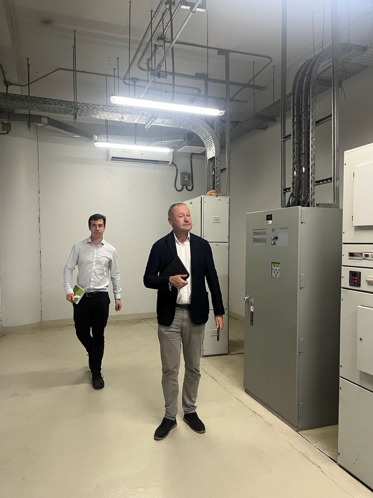 Two of the HarmoniQ team walking through a shopping centre’s switchroom, switchgear cabinets on the right