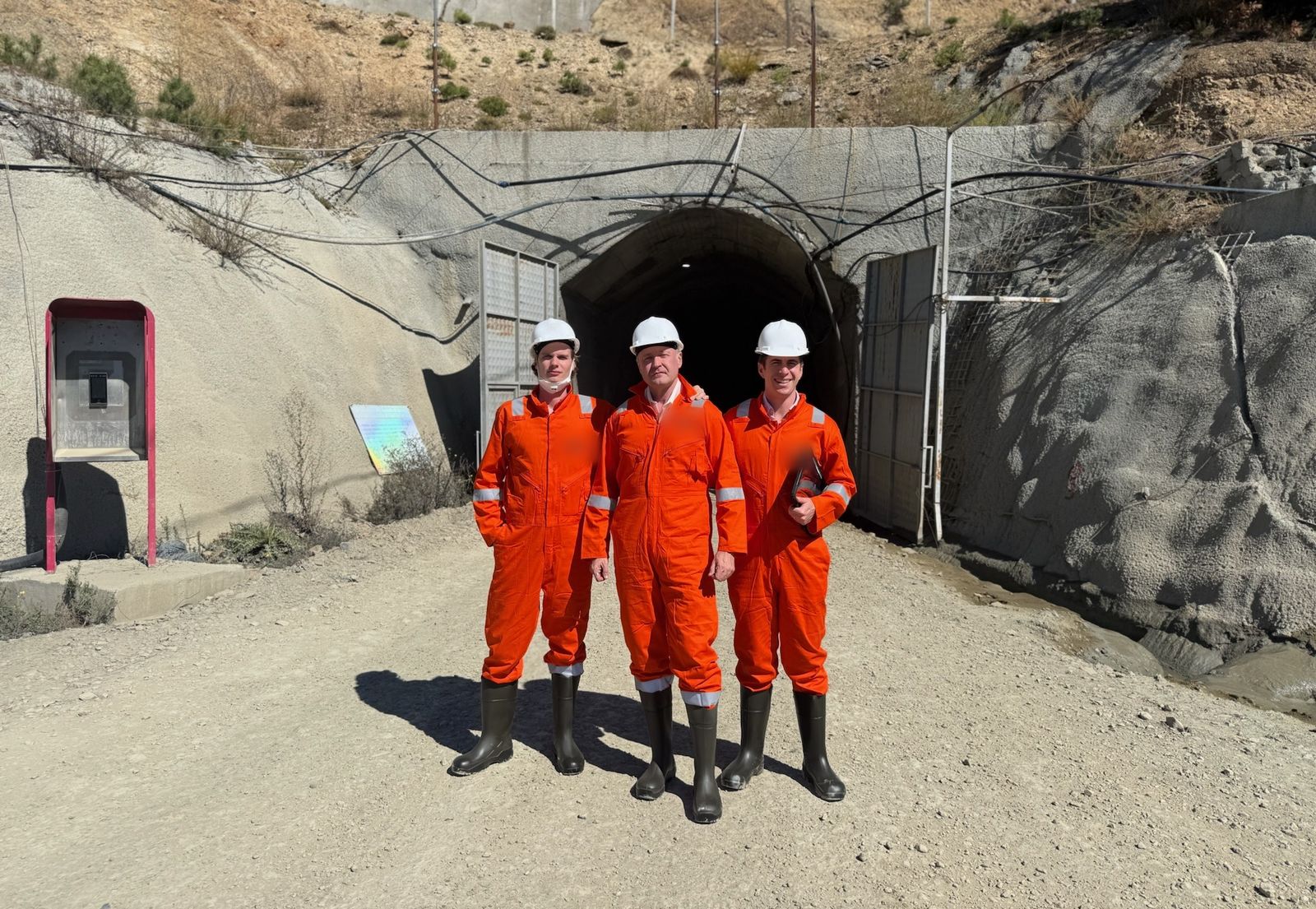 Three of the HarmoniQ team in orange coveralls and hard hats at the entrance to a mine tunnel