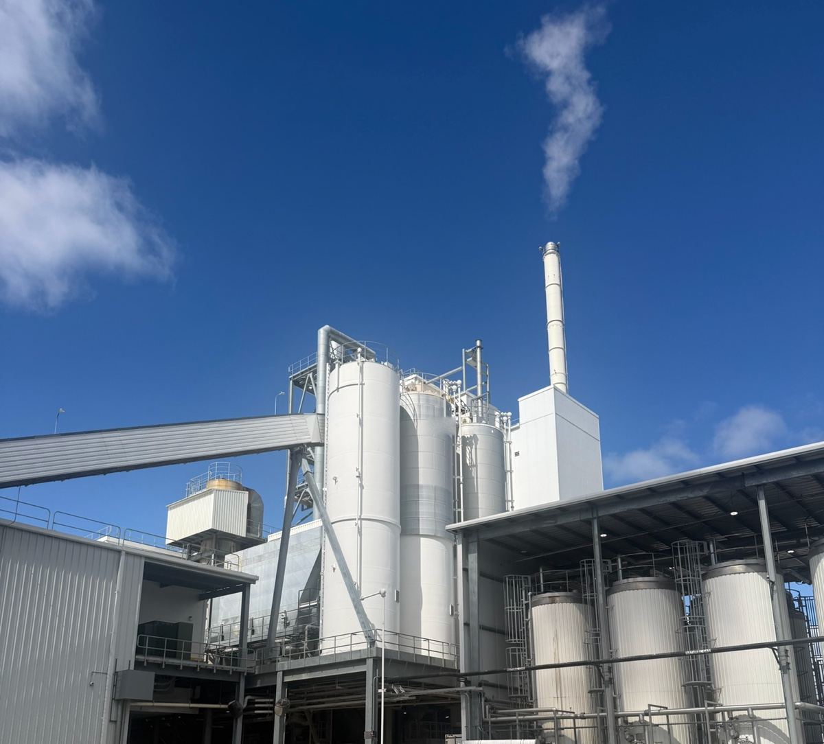 The silos and stack of an insulation plant against a deep blue sky