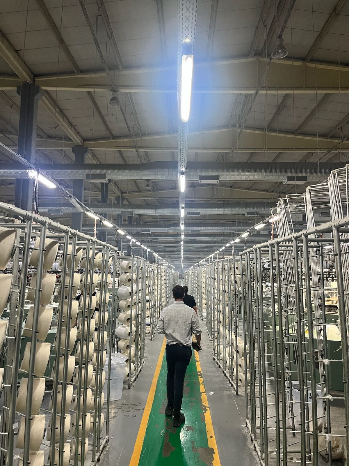 A long aisle between spinning frames in a textile mill, two people walking away down it