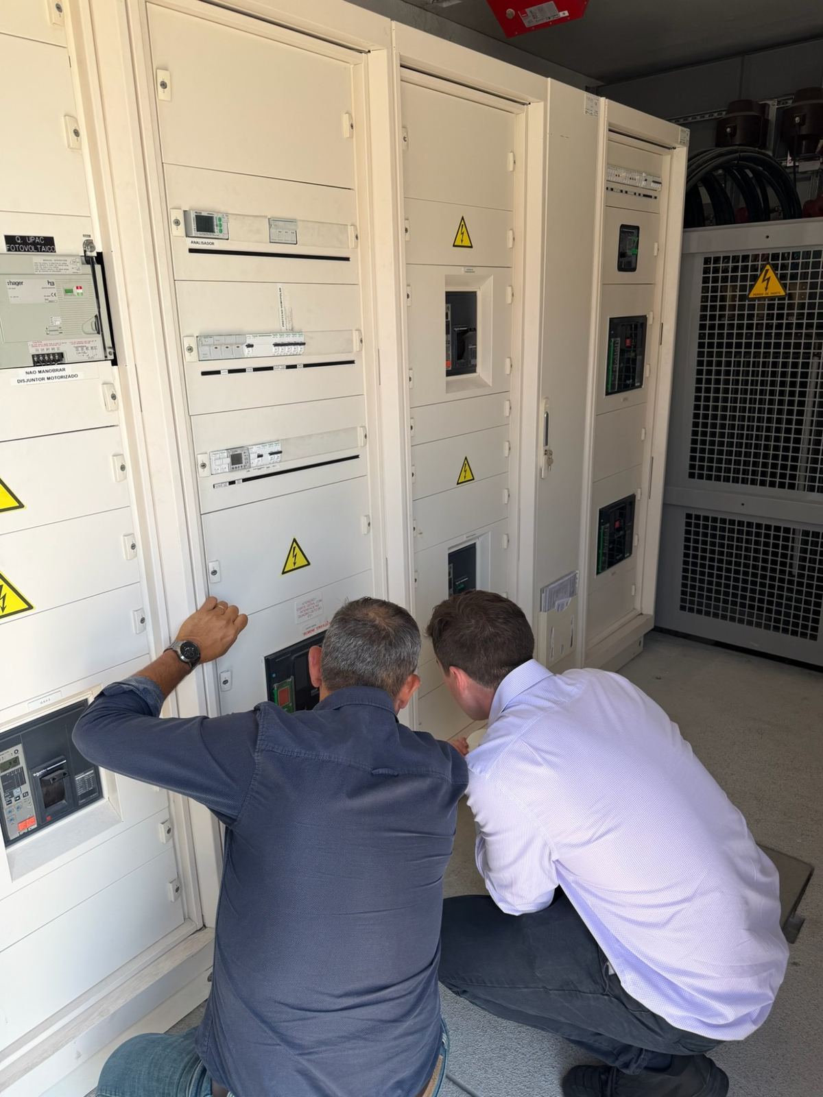 Two people crouching to inspect the lower section of a main switchboard